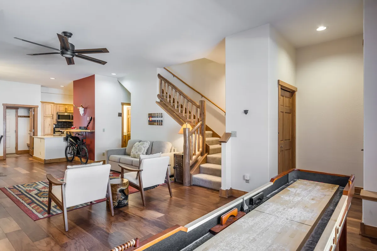 An inviting open-concept living space with a visible game table, cozy sofa, kitchen area, and staircase. The layout encourages social gatherings, playing games, and relaxed family time, reinforcing the home’s kid-friendly design.