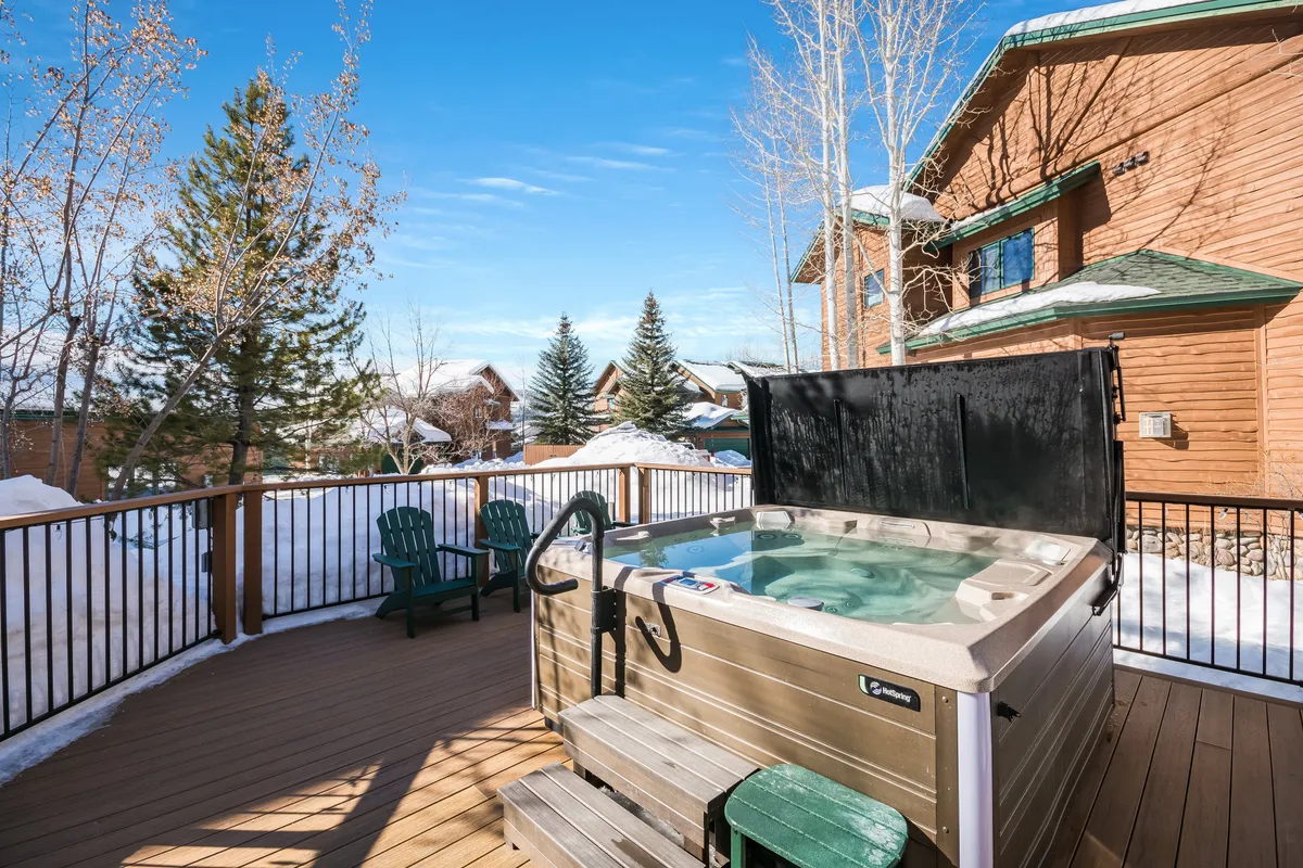 This exterior image captures a steaming hot tub surrounded by deck chairs, set against a backdrop of snowy ground and tranquil trees. The inviting scene suggests a perfect après-ski setting where guests can relax after a day on the slopes, enjoying the crisp mountain air and natural beauty.