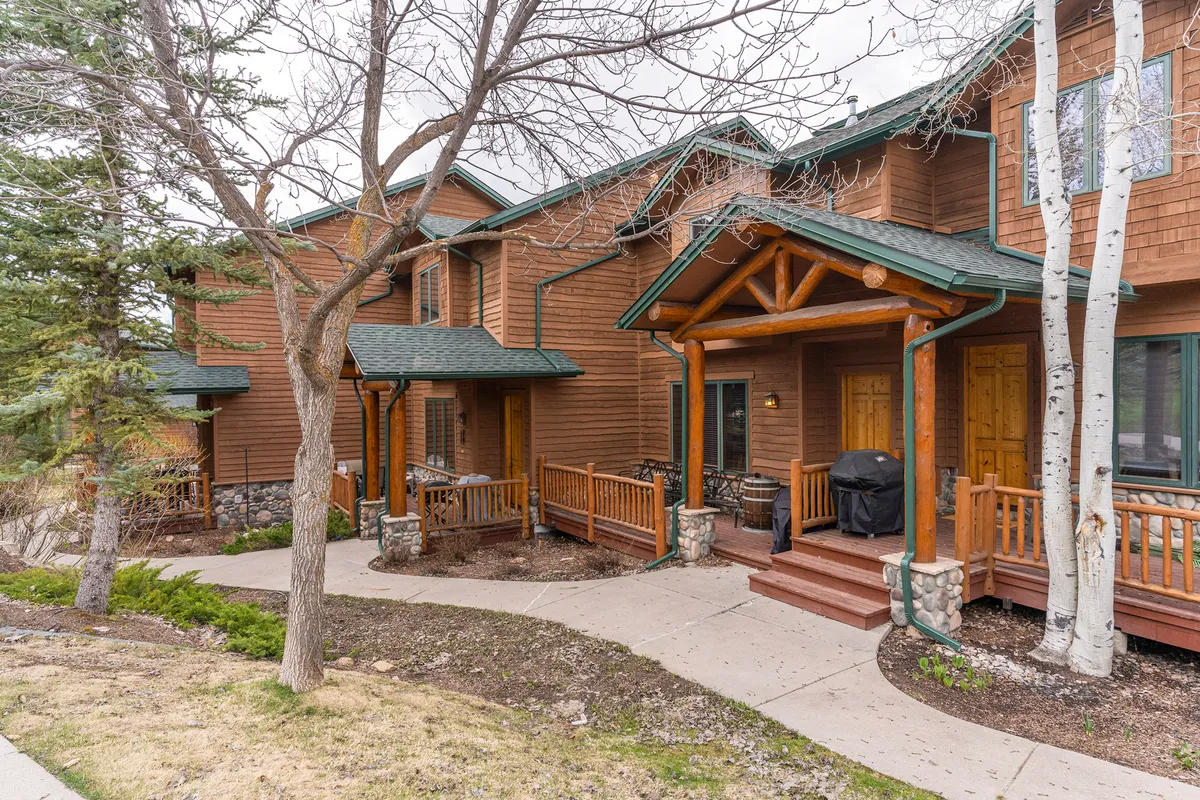 This exterior shot features charming wooden front porches with stone accents and aspen trees lining a pathway. The cozy, residential setting highlights the tranquil neighborhood environment and the inviting outdoor spaces where guests can gather or enjoy peaceful moments before or after their alpine adventures.