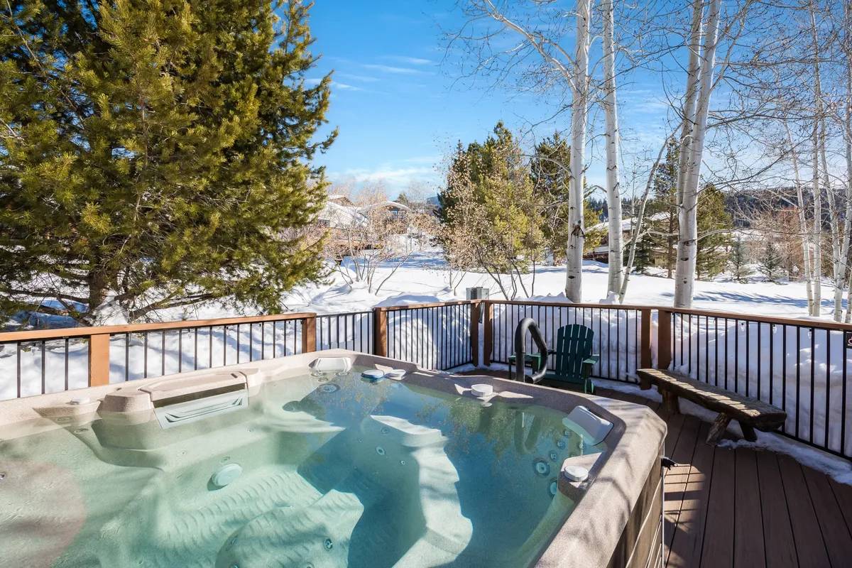 An exterior shot of the private deck featuring a wooden deck, BBQ grill, hot tub, and surrounding snowy landscape. The tranquil setting hints at both lively outdoor gatherings and quiet moments amidst nature.