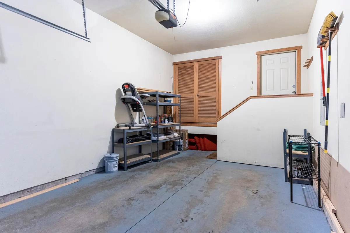 Inside the garage, shelves are lined with tools and equipment, and there is a treadmill and stairs leading to a door. The space is tidy and organized, emphasizing its functionality for gear storage and preparation for outdoor activities.
