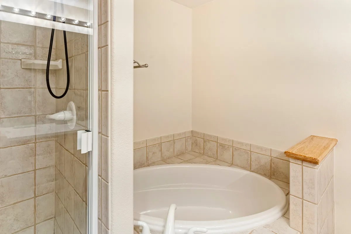 A serene, spa-like bathroom featuring a large jacuzzi tub, modern shower enclosure, smooth tiles, and a wooden ledge for toiletries. The space is designed for luxurious self-care routines and unwinding after a long day, with natural light enhancing the tranquil mood.
