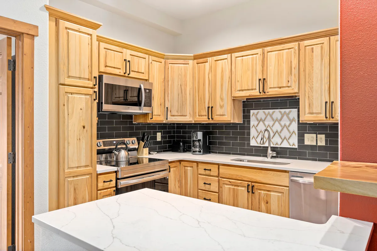 A modern kitchen with wood cabinetry, marble countertops, a black backsplash, and stainless steel appliances. The layout is open and ideal for hosting, cooking, and sharing meals, blending seamlessly with the surrounding spaces.