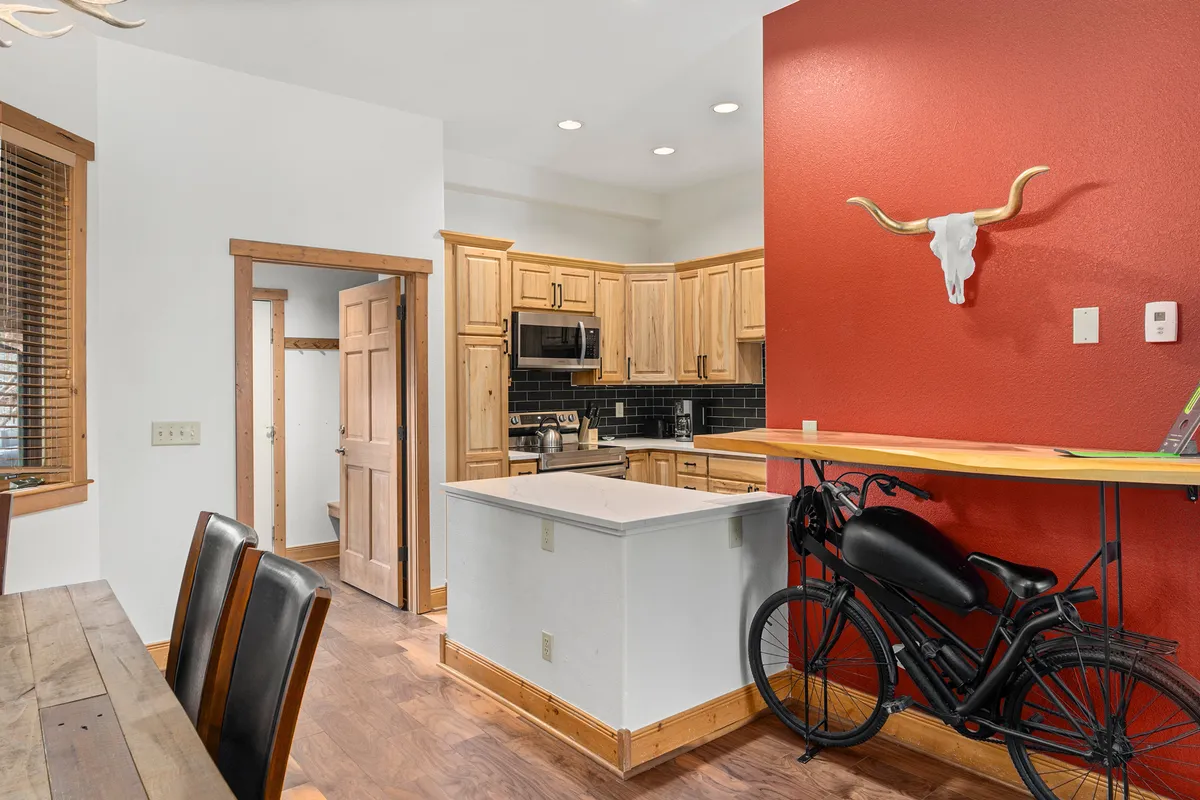 A cozy interior view showing kitchen cabinetry and a red accent wall, with a bicycle on a stand in the foreground. The presence of the bike emphasizes indoor storage and the adaptable use of living spaces for mountain gear.