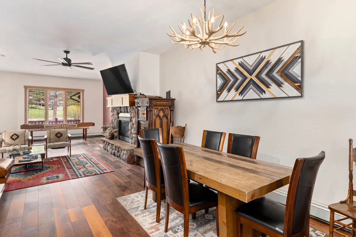 A cozy dining area featuring a large table, a glowing fireplace, and a chandelier, inviting guests to share meals or enjoy game nights. The scene exudes warmth and camaraderie.